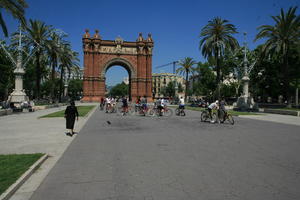 architecture, archway, Barcelona, bright, Cataluña, cycling, day, direct sunlight, eye level view, group, lamppost, palm, people, Spain, spring, street, sunny