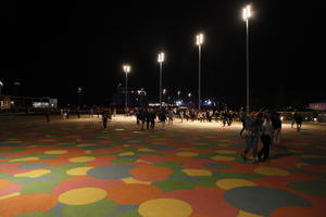 artificial lighting, casual, England, eye level view, group, London, night, outdoor lighting, pavement, people, square, stadium, summer, The United Kingdom, walking