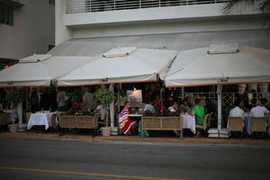 building, cafe, canopy, chair, crowd, dusk, eye level view, Florida, Miami, object, people, potted plant, sitting, standing, street, summer, table, The United States, vegetation, winter