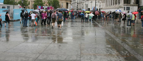 ambient light, casual, day, diffuse, diffused light, England, eye level view, group, London, passerby, people, plaza, square, summer, summer, The United Kingdom, umbrella, walking, wet