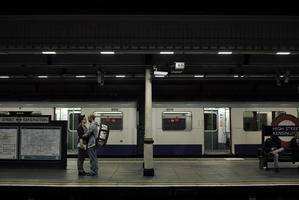 artificial lighting, couple, England, eye level view, hugging, London, night, people, side, standing, station, The United Kingdom, train